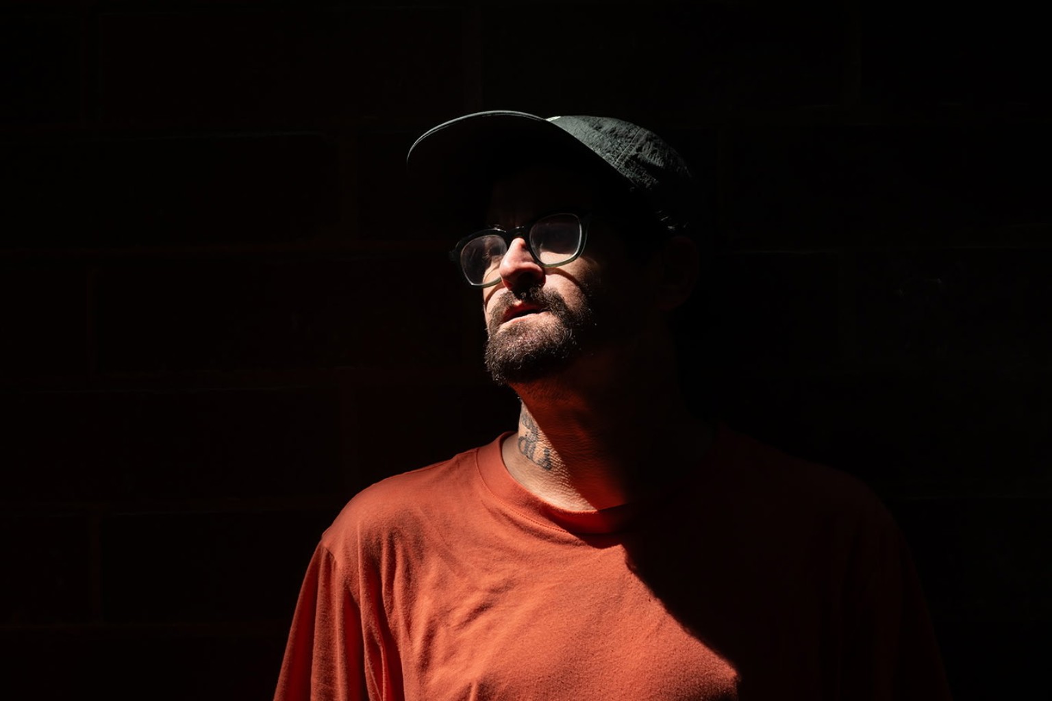 Seth Stolz in a dramatic portrait wearing an orange shirt and cap